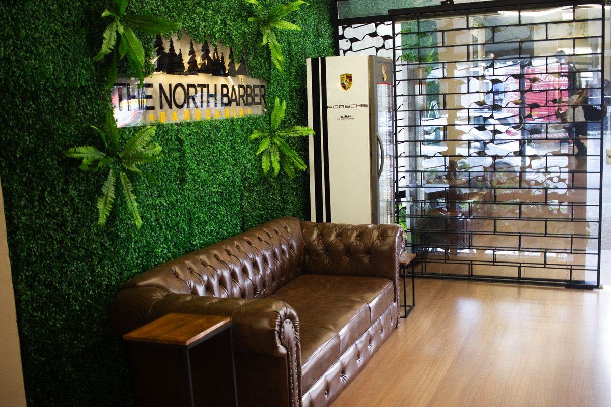Sofá de couro chesterfield em frente à parede verde na entrada da The North Barber